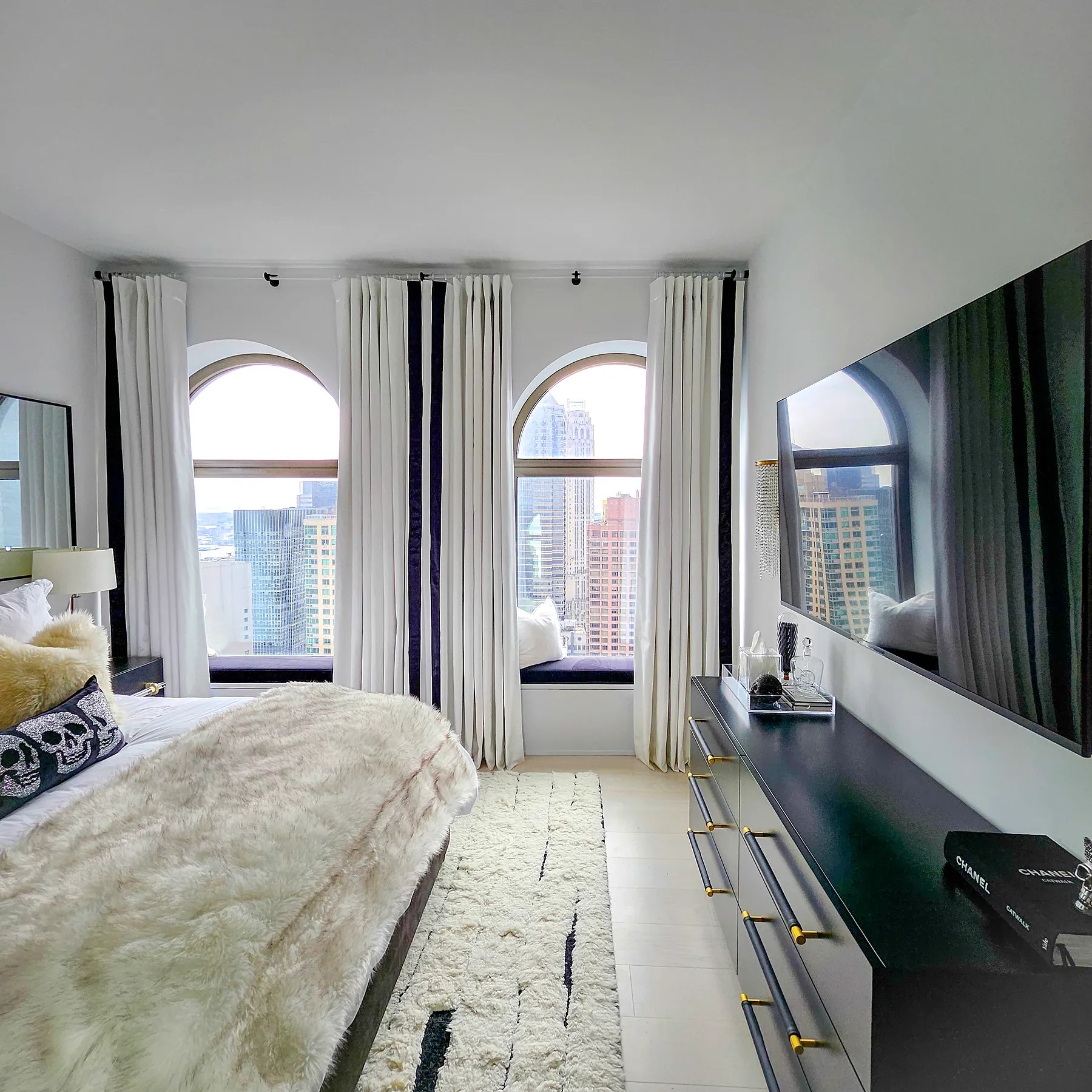 Pinch pleat drapery with contrast leading-edge banding across arched bedroom windows