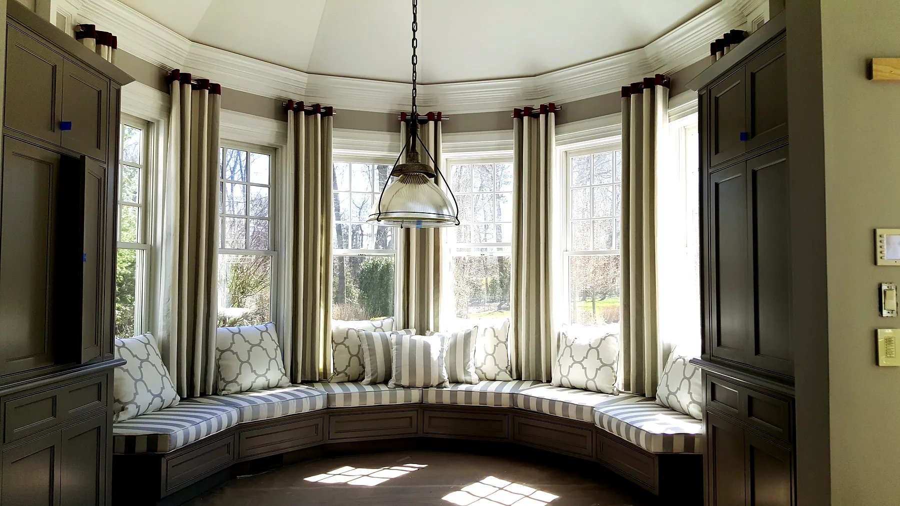 Striped grommet drapery panels between windows in a curved bay with built-in bench seating