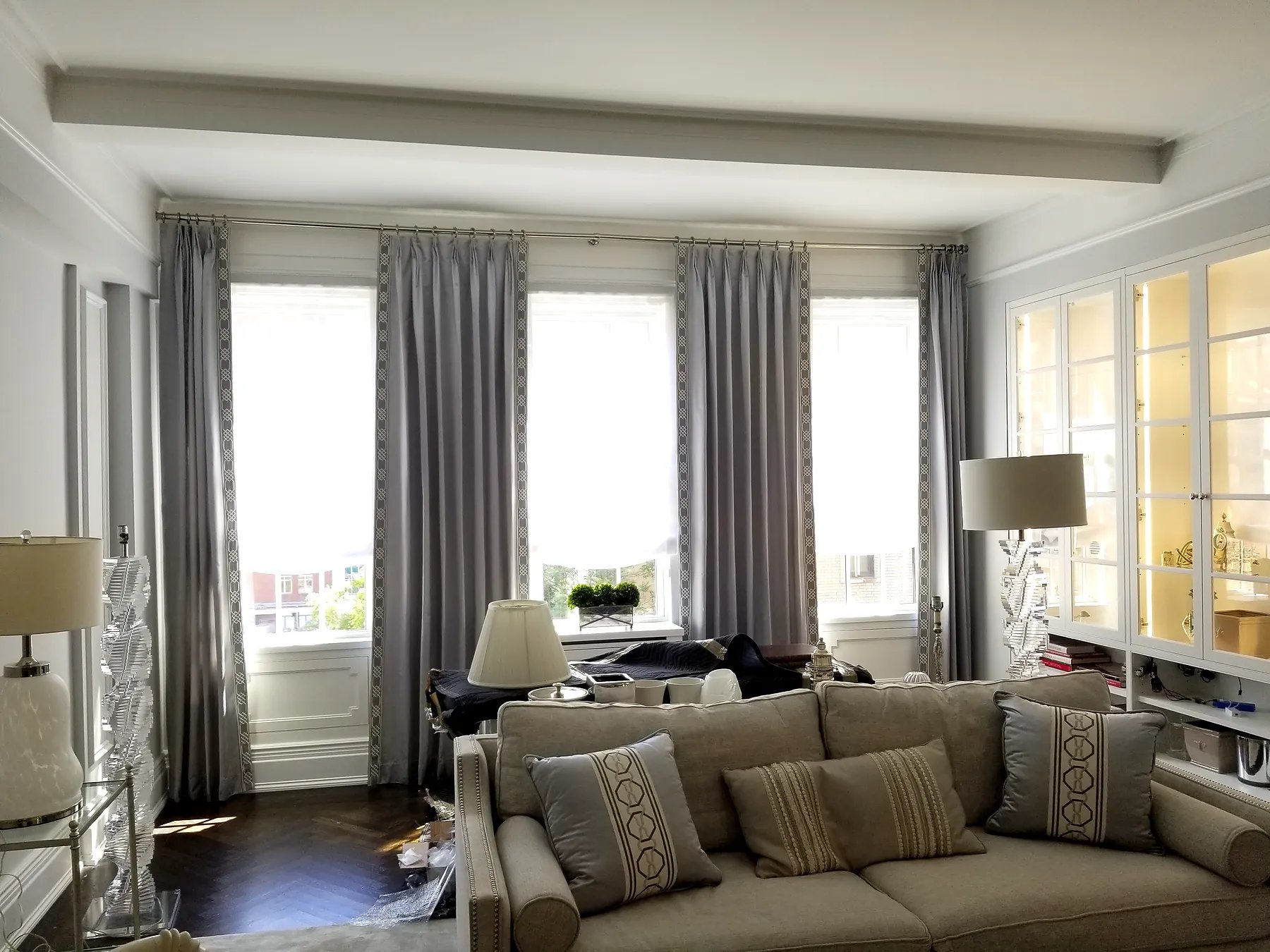 Pinch pleat drapery with decorative trim banding on leading edges across three windows