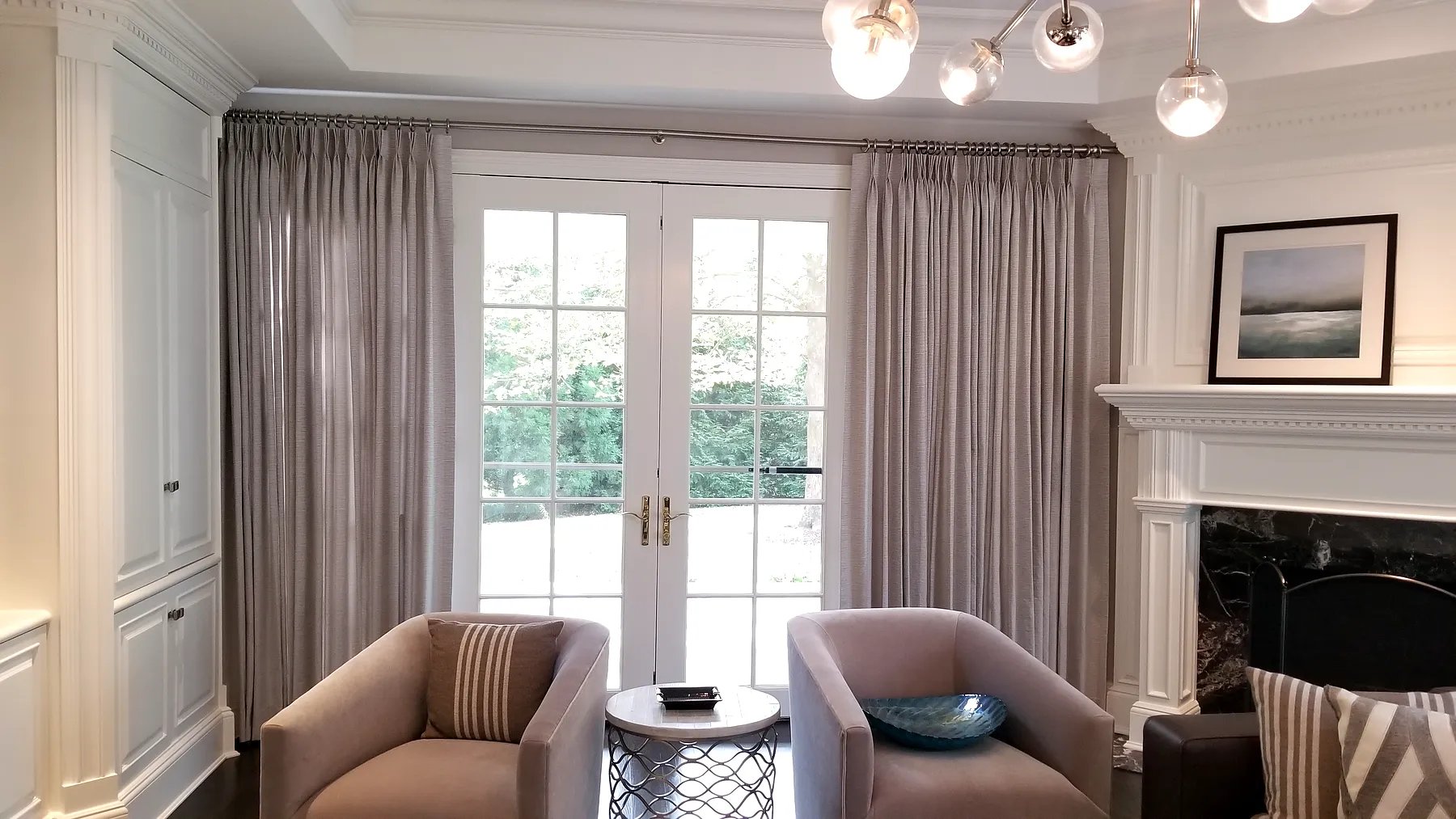 Pinch pleat drapery flanking French doors in a formal sitting room with fireplace
