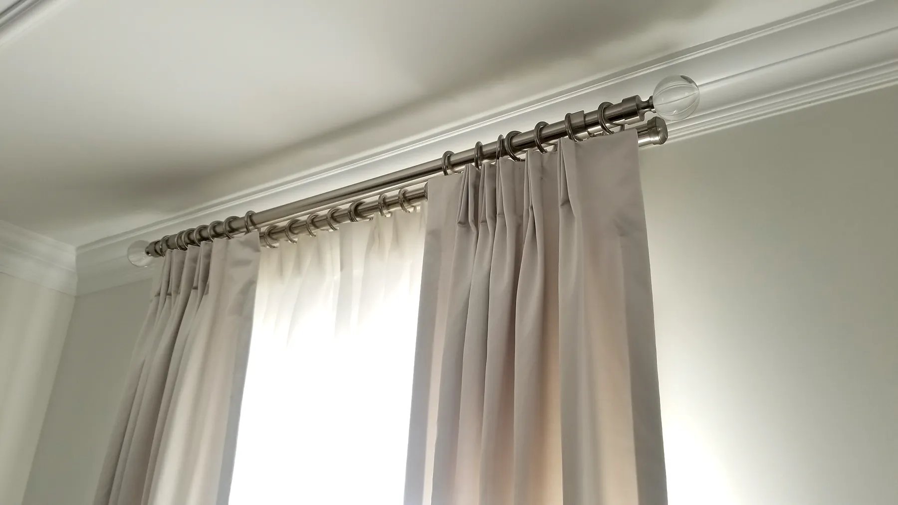 Close-up of pinch pleat drapery header with metal rod, rings, and decorative finial