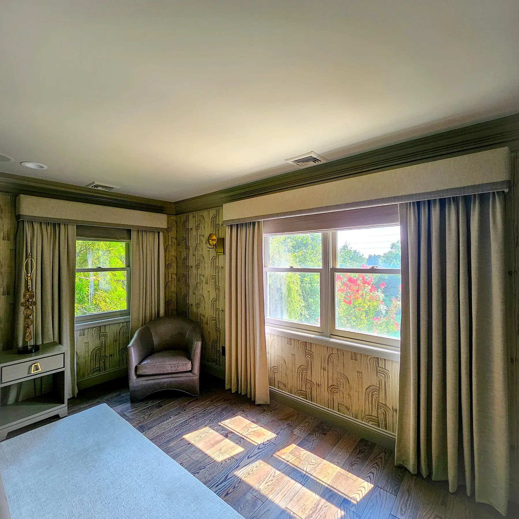 Upholstered cornice valances over drapery on two windows in a patterned-wallpaper bedroom