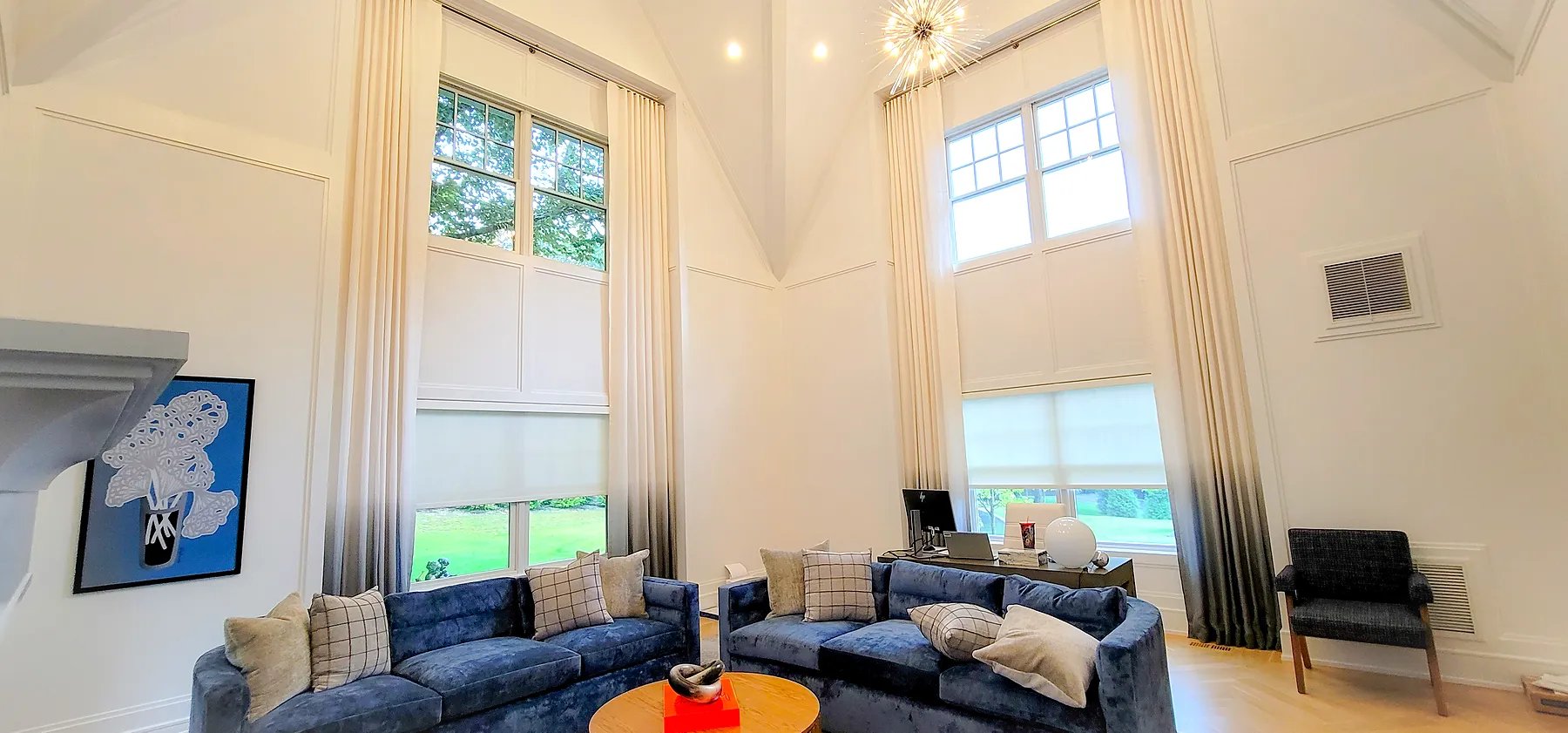 Tall ombré drapery layered over roller shades in a two-story great room