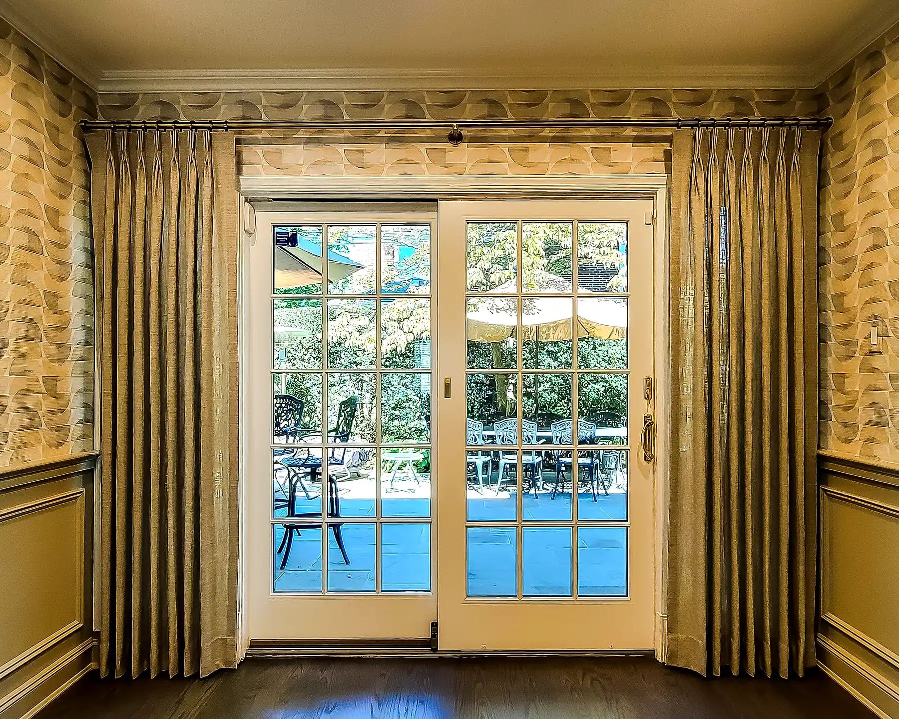Pinch pleat drapery flanking French doors to a patio, paired with patterned wallpaper