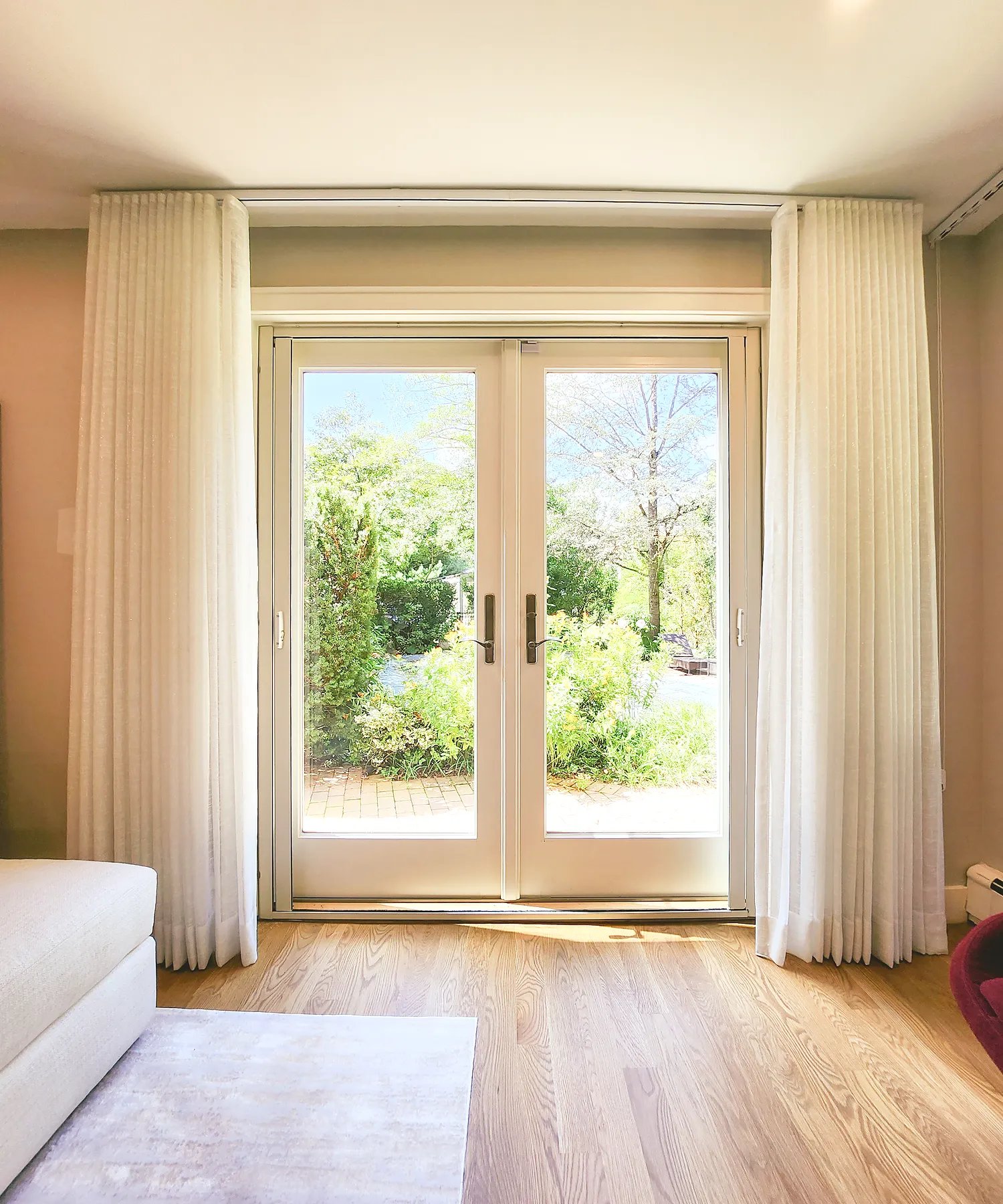 Sheer ripplefold drapery flanking French doors to a garden