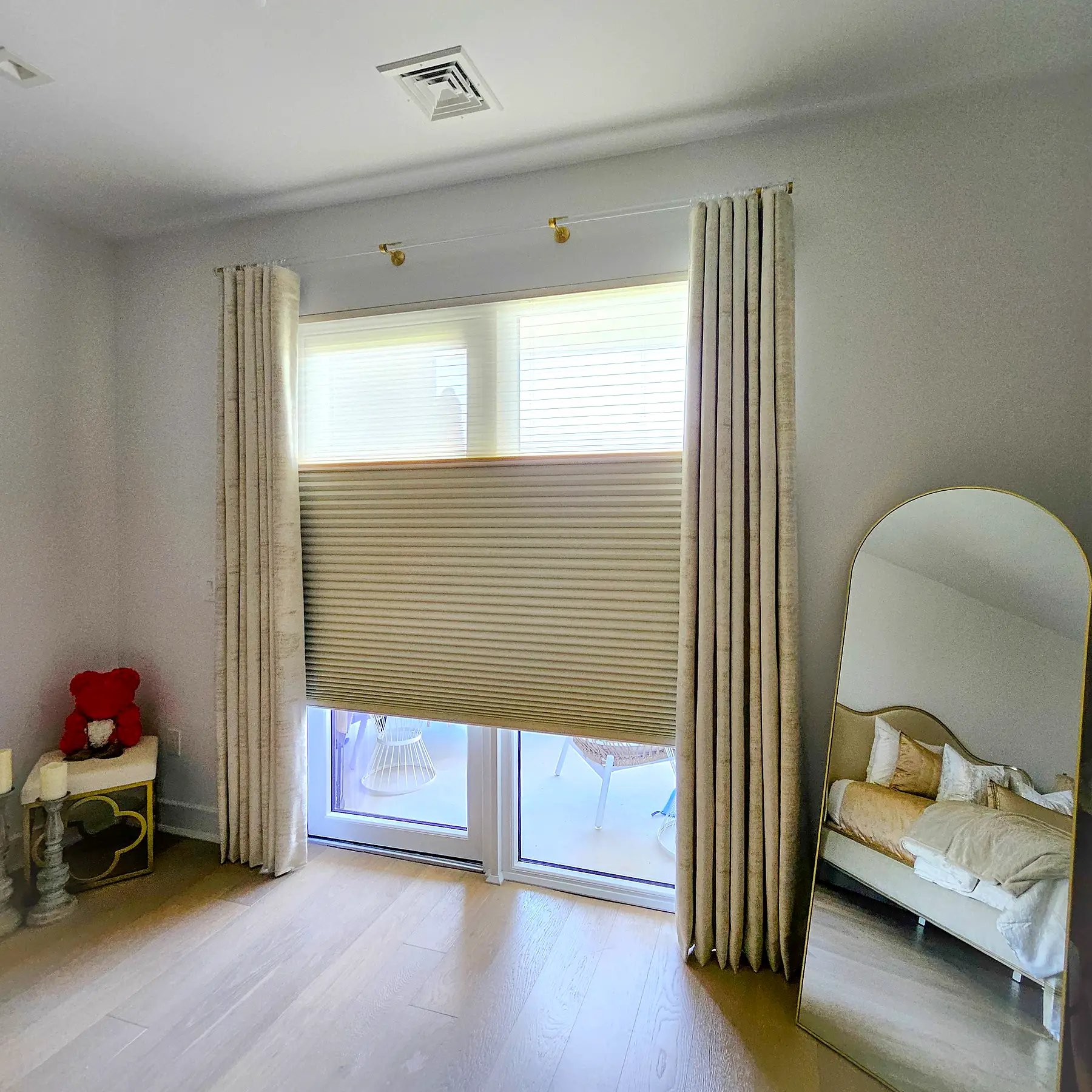 Pleated drapery side panels layered over top-down cellular shades on a sliding door